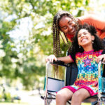 Little girl in a wheelchair at the park with her mother.