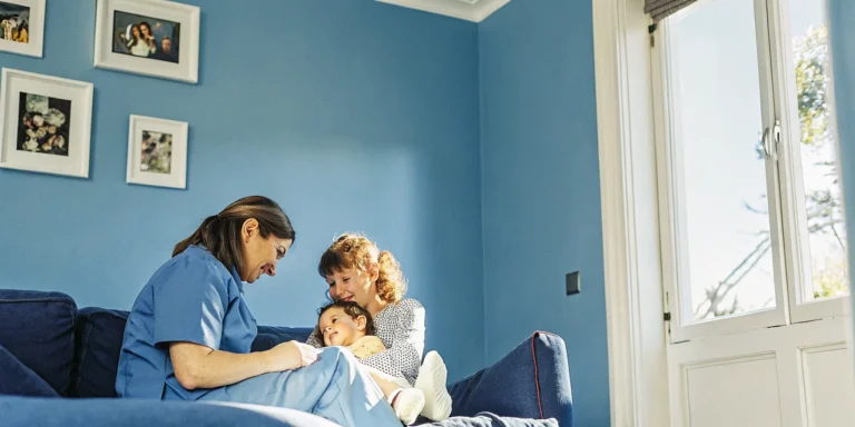 Pediatric nurse caring for a child at home with family nearby in a warm, comfortable setting